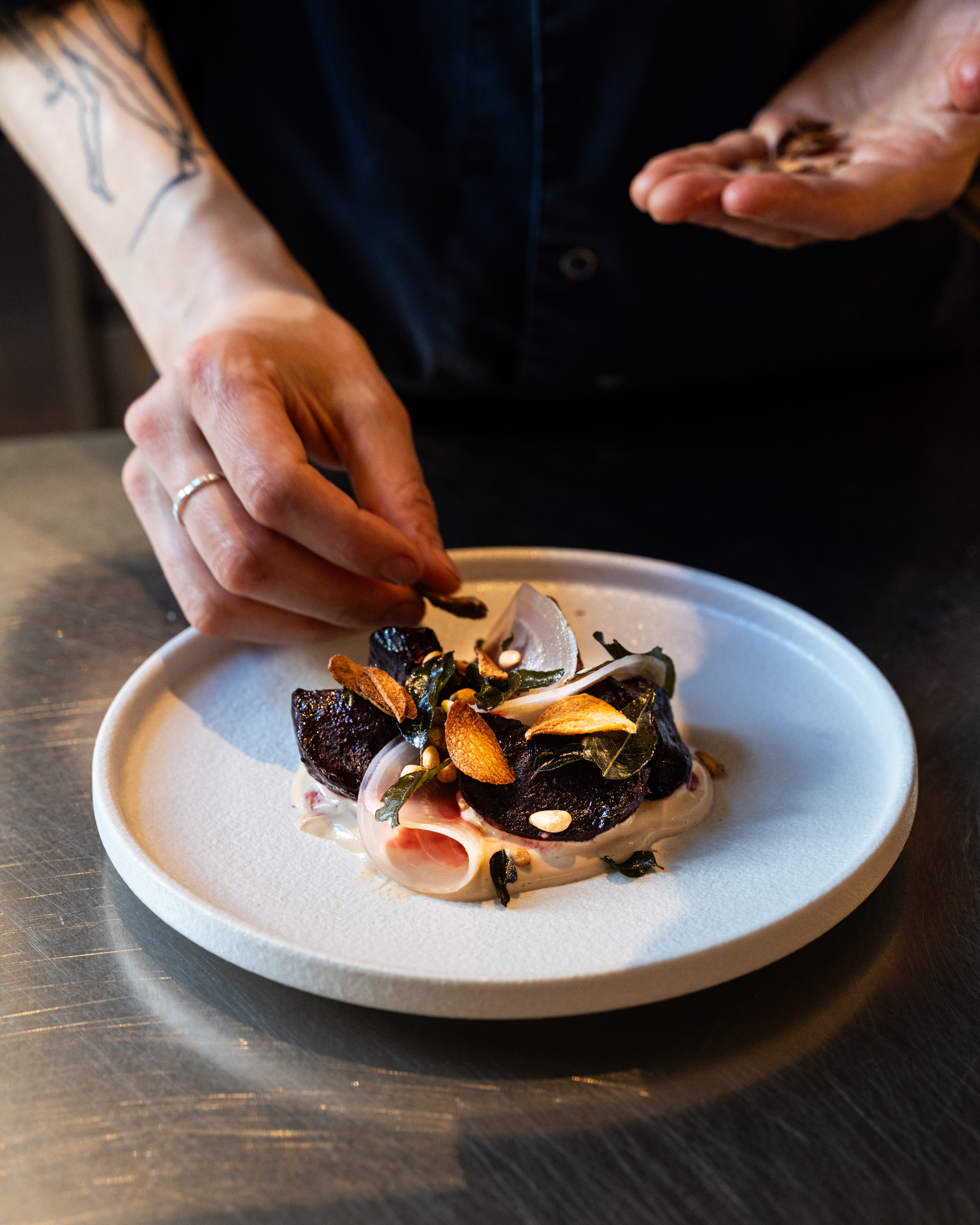 Close up of a dish with hand adding small orange leaves as a topping.
