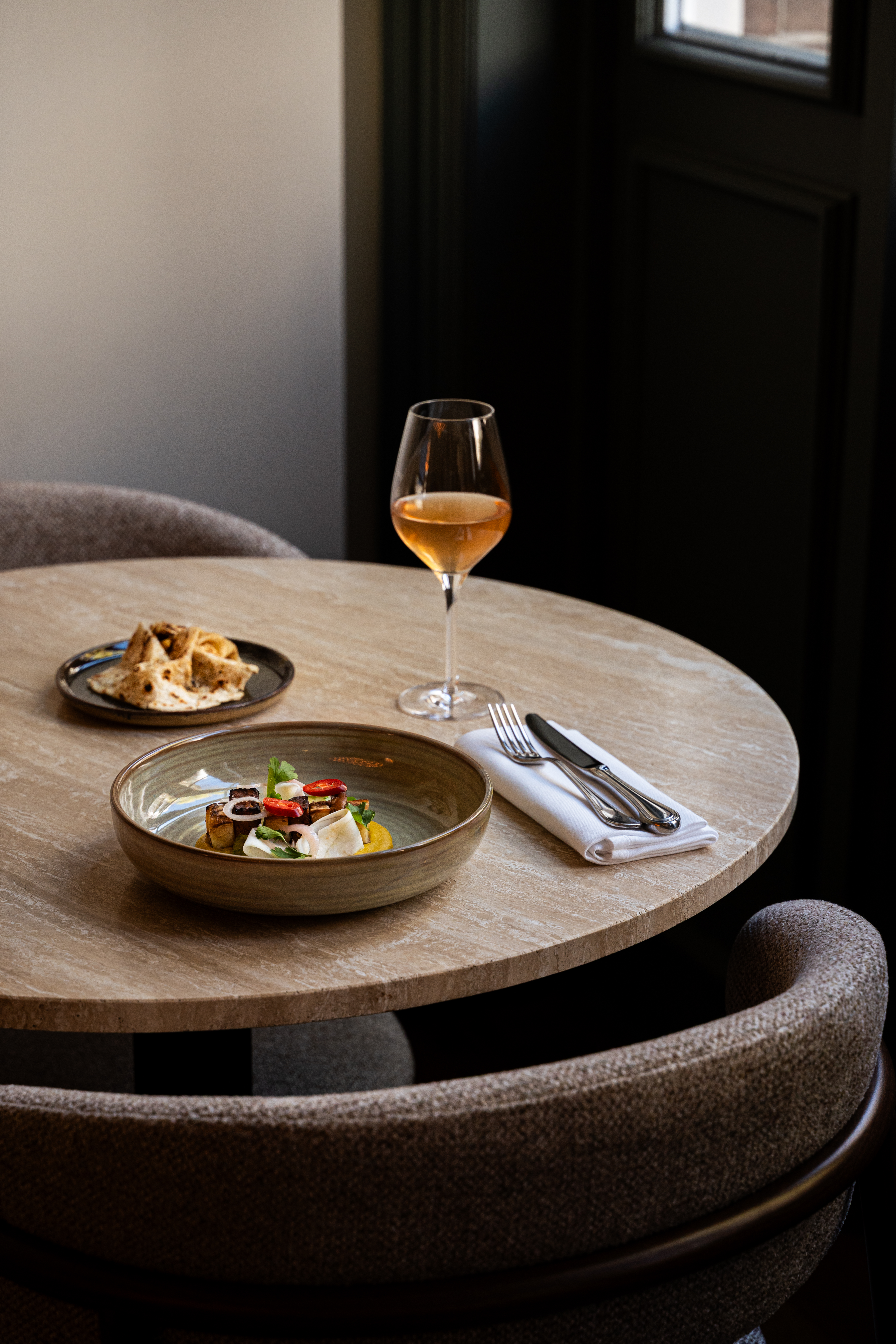 Table in a restaurant with a dish, side dish, cutlery on a white folded napkin and a wine glass with plum wine.
