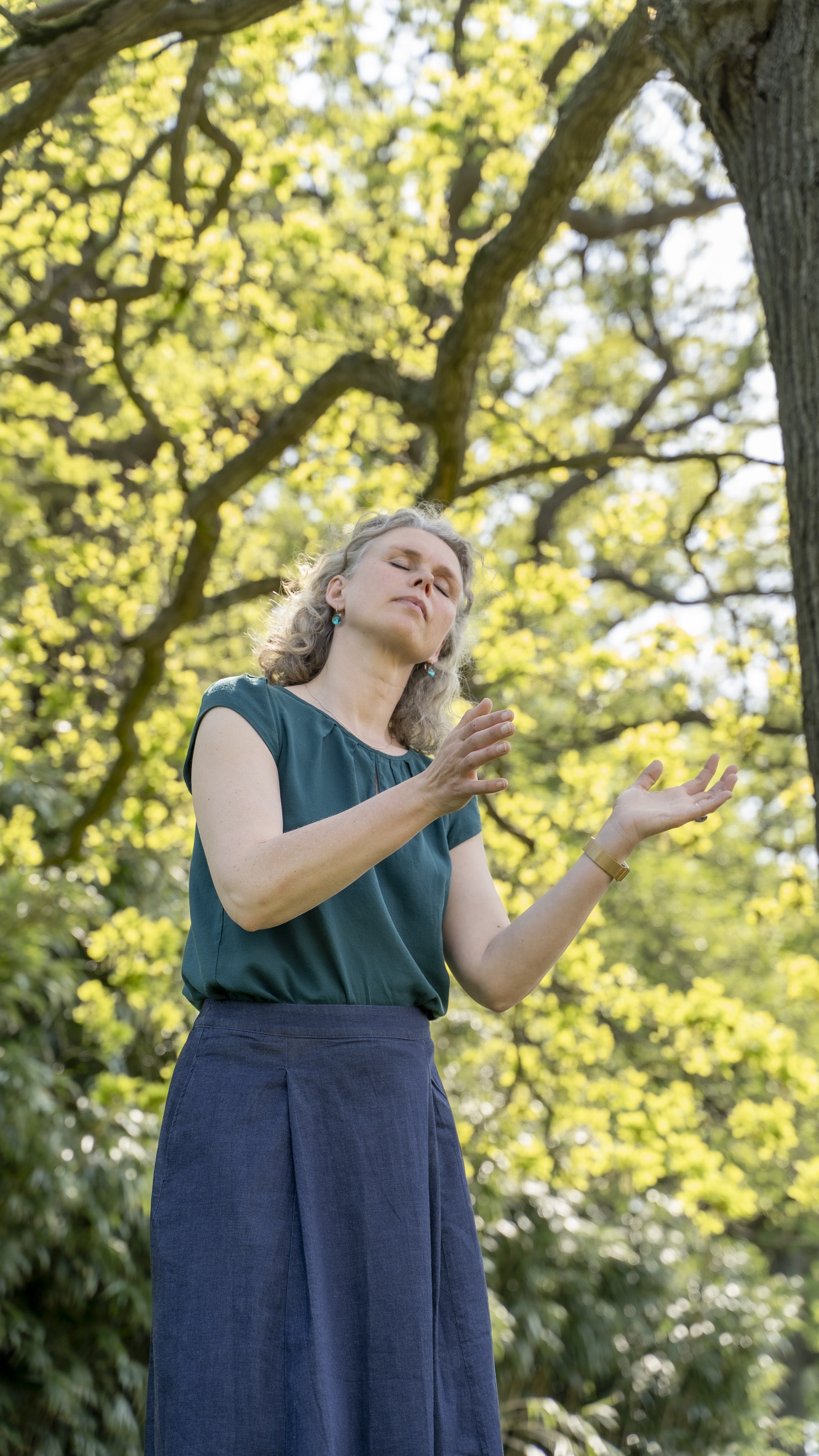 Woman dancing slowly under a tree with her eyes closed.