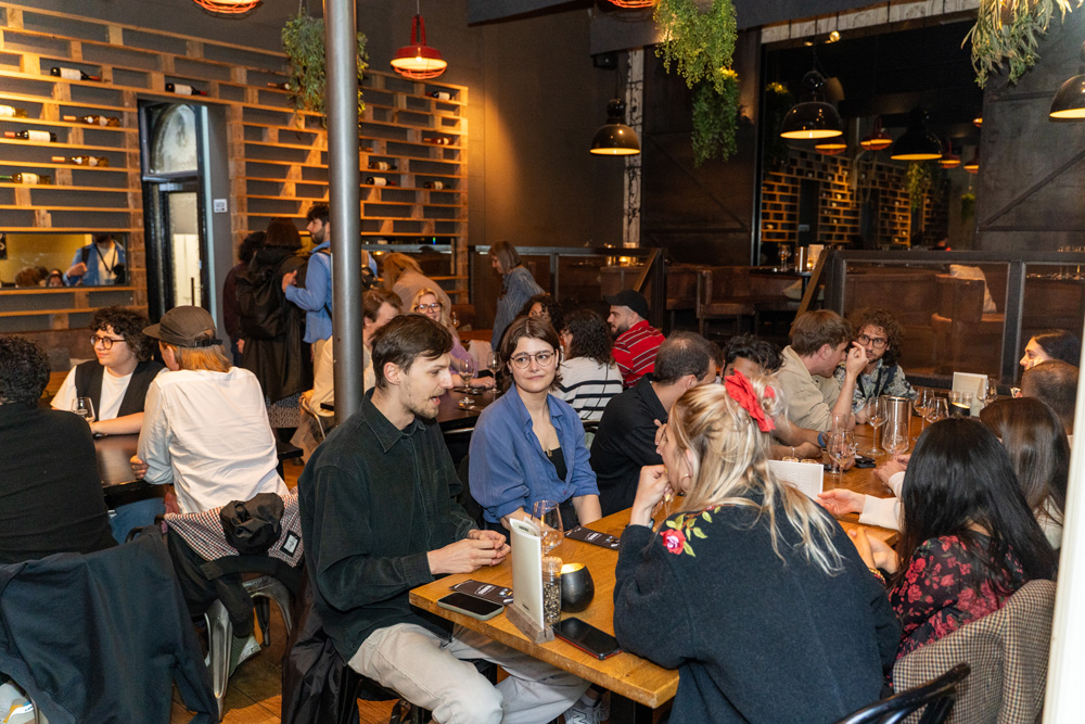 Big group of people sitting at different long tables networking together.