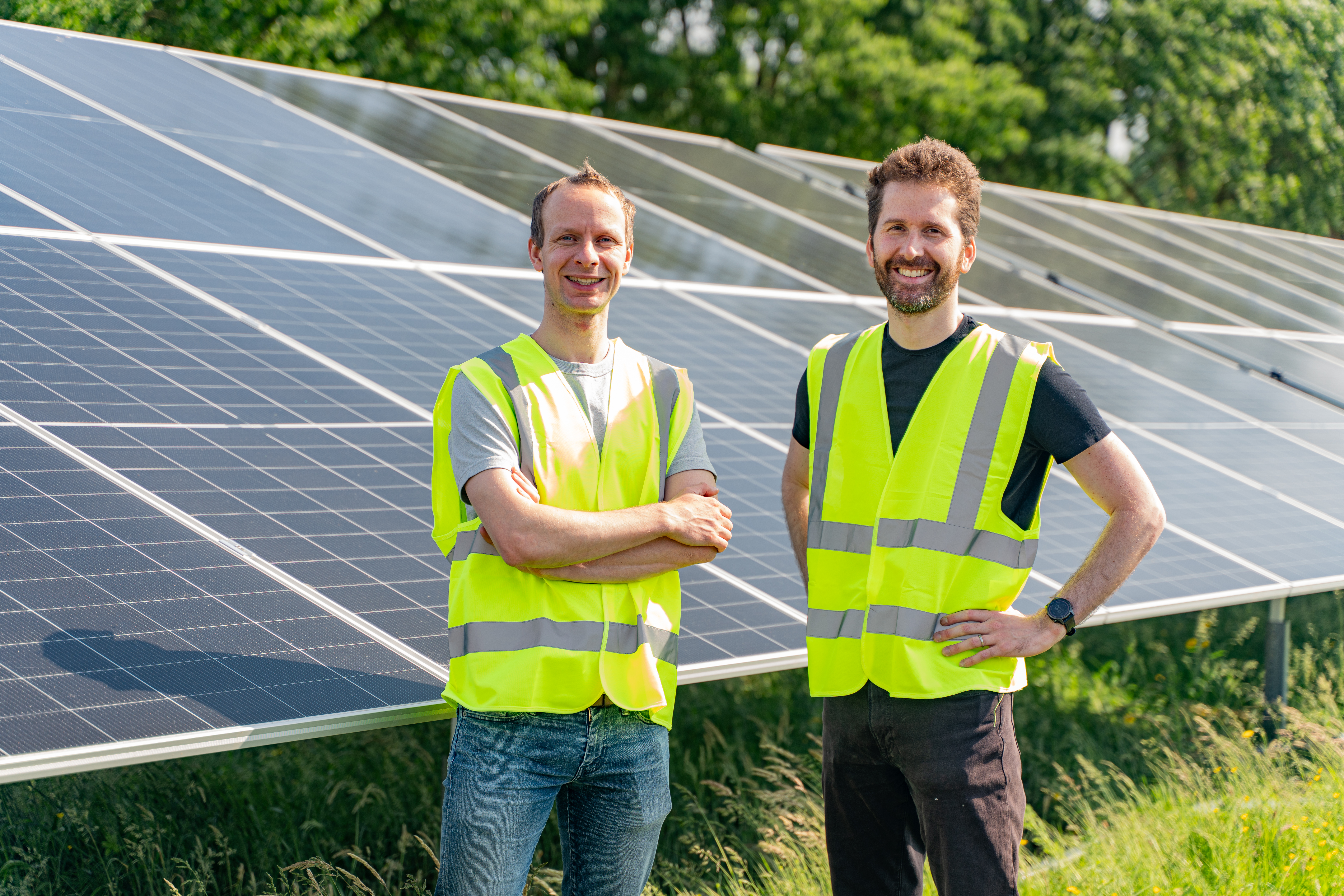 Two men wearing fluorescent vests standing in front of solar panels