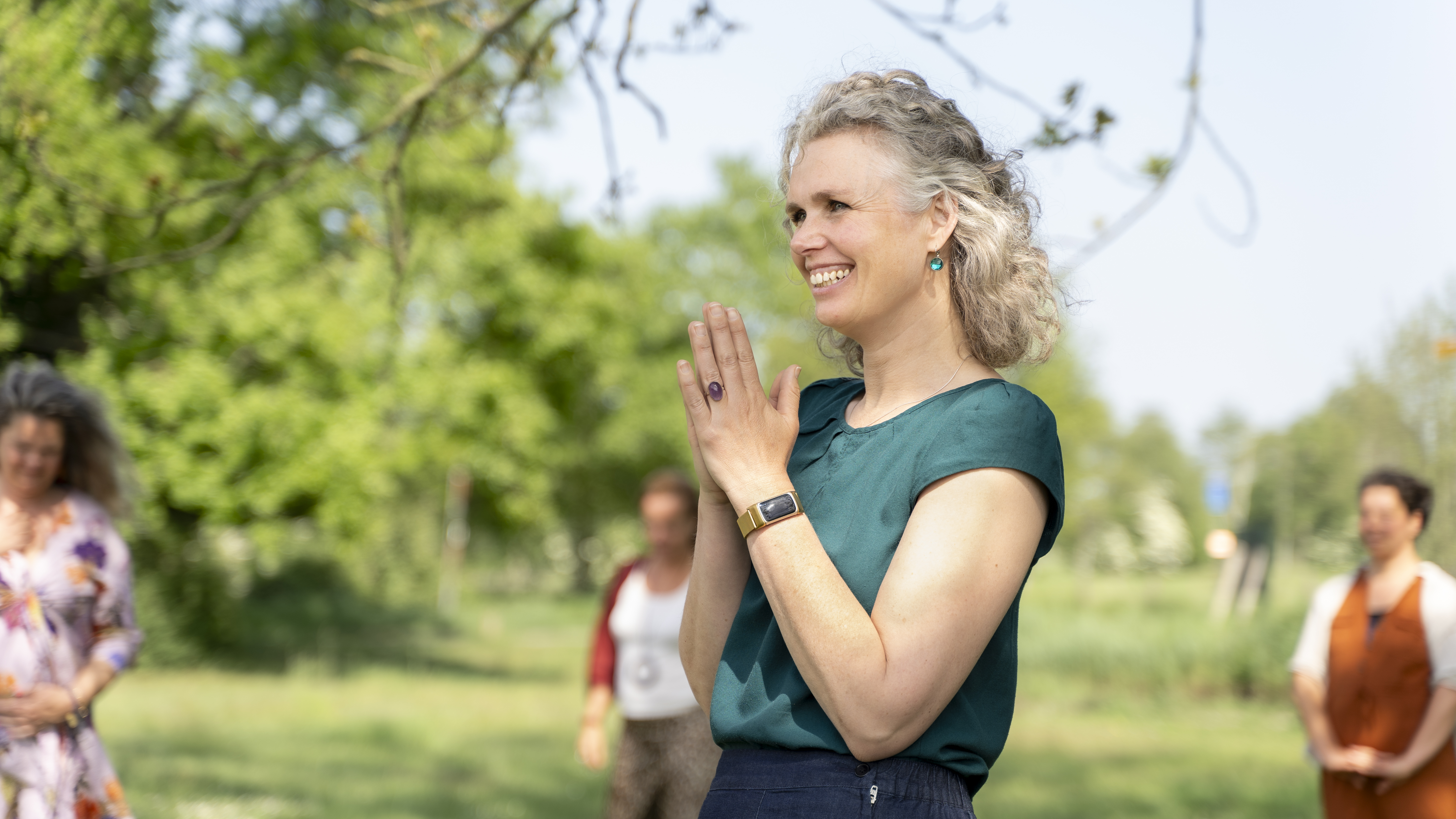 Woman standing outside smiling and holding her hands in prayer.